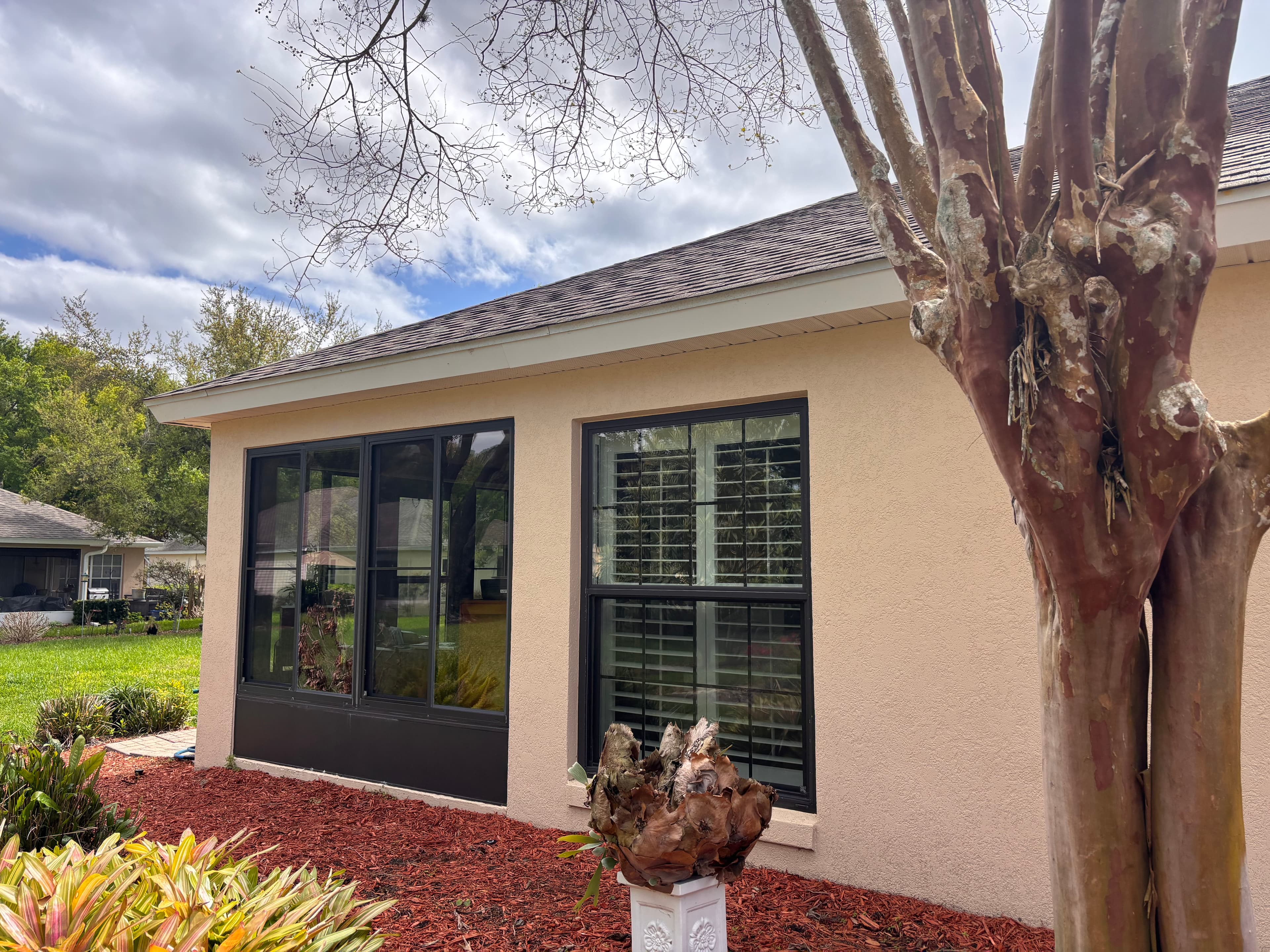 Tan house with black windows, red mulch, and a large tree trunk in the foreground.