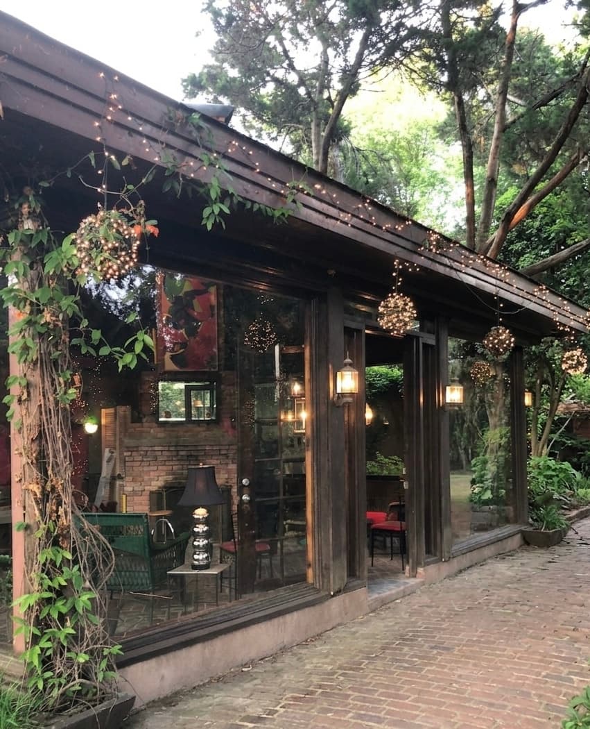 Rustic wooden building with large windows, fairy lights, and hanging glowing orbs on brick patio.